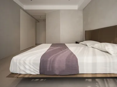 A minimalist bedroom featuring concrete walls, fabric bedding, and wood accents.