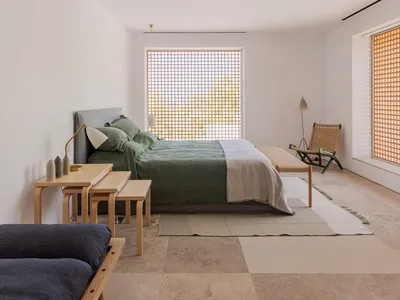 A minimalist bedroom featuring wooden furniture and light-colored bedding with a view of nature through the window.