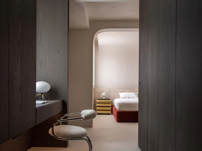 A minimalist bedroom with dark wooden walls and furniture, featuring a white bed and a modern chair.