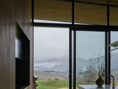 現代極簡住宅廚房，配有大型玻璃窗，可俯瞰綠意盎然的山丘與山景。
