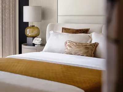 A modern minimalist bedroom featuring a wooden floor, white and gold bedding, and a white lamp with a gold base.