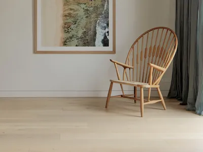 A minimalist living room featuring a wooden armchair and a framed abstract beachscape on the wall.
