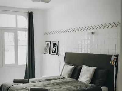 Modern, minimalist bedroom with a white bed frame, upholstered headboard, green bedding, and white tile walls