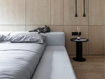 A serene modern bedroom featuring a gray upholstered bed with light wood paneling on the walls and a small side table.