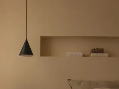 A minimalist bedroom featuring fabric bedding, wooden furniture, and metal accents on a bed with a window and a black pendant