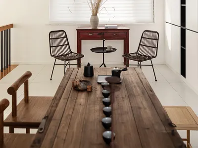 A minimalistic living room featuring a wooden table with black ceramic tea cups and a white vase with dried plants by the win