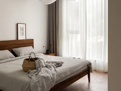 A minimalist bedroom featuring a bed with white curtains and a wooden headboard, minimalistic decor, and a serene atmosphere.
