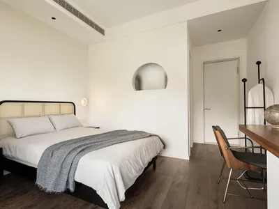 Modern minimalist bedroom with a white bed, grey throw blanket, and wooden floor.