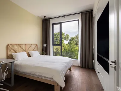 A minimalist bedroom featuring wooden furnishings, white bedding, and large windows.