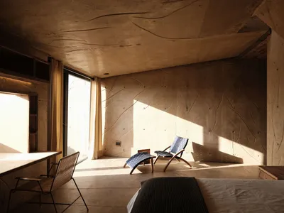 A minimalist bedroom with concrete walls, bench seating, and a bed.