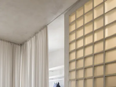 A minimalist bedroom featuring a glass-enclosed wardrobe, white furniture, and wooden flooring.
