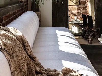 A cozy living room featuring a white sofa, a green plant, and brick walls