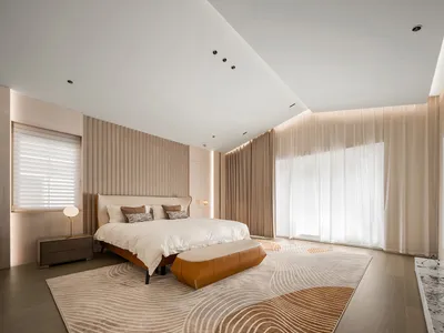 A modern bedroom features a brown leather bed, white curtains, and a patterned rug.