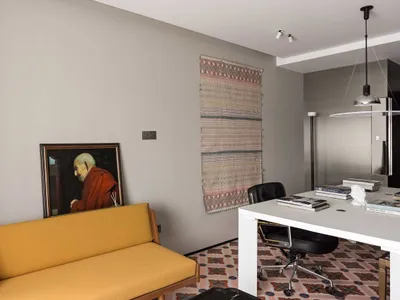 A modern home office setup featuring a yellow sofa, a desk with books and reading materials, and a hanging light fixture.