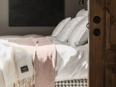 A minimalist bedroom with a wooden door, white bedding, and soft textiles.
