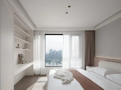 A modern minimalist bedroom featuring white fabric bedding and wooden elements.