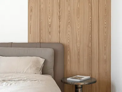 Minimalist bedroom with a bed, wooden wall paneling, and a bedside table with a book.