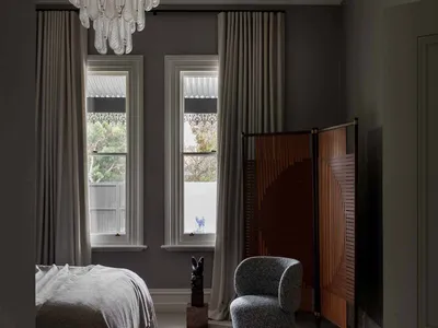 A minimalist bedroom with grey walls, a grey bed, and a grey carpet, featuring a stylish chandelier and decorative screens.