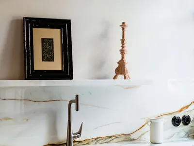 A minimalist kitchen with a white marble countertop featuring a stainless steel faucet and a white ceramic mug.