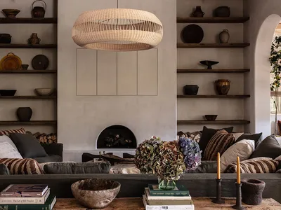 A minimalist living room with a wicker pendant light, shelves adorned with various ceramics, and a dark sofa.