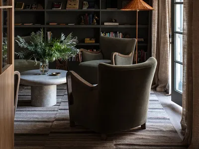 Industrial living room featuring plush green armchairs, glass lampshade, bookshelves, and green plants