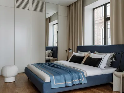 Modern minimalist bedroom with a blue upholstered bed, white linens, and black lamps.