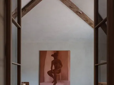 A minimalist bedroom with a canvas bedspread and textile accents, featuring a portrait painting of a seated figure.