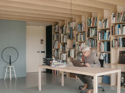 A modern home office featuring a wooden table and floating shelves filled with books.