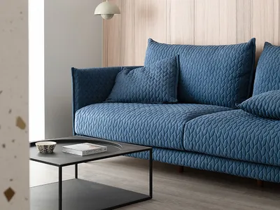 A blue sofa in a minimalist living room featuring a modern design with wooden walls and a pendant light fixture.