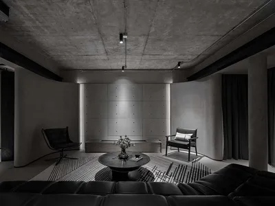 Modern industrial-themed living room with concrete walls and black leather furniture.