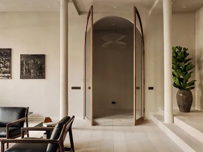 A minimalist living room with beige walls, wooden flooring, and a plant in a vase on a step.