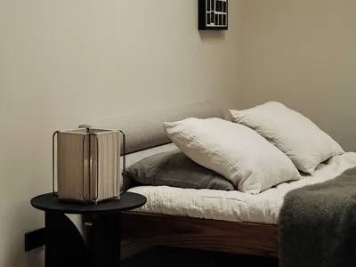 A minimalist bedroom featuring a wooden bed frame and white linens.