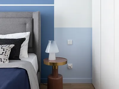 A minimalist bedroom featuring a bed with a wooden headboard and blue and white bedding, accompanied by a side table with a t