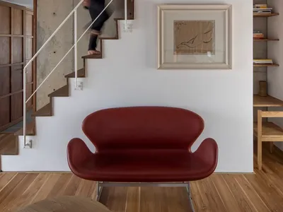 A contemporary living room with concrete walls, stairs, and a red sofa.