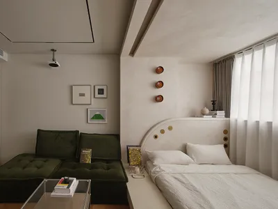 A minimalist bedroom featuring a green upholstered couch, a white bed with a curved headboard, framed art on the wall, and a