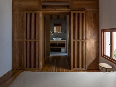 A minimalist bedroom featuring wooden elements, a wooden bed, and a wooden cabinet with a sink and mirror.