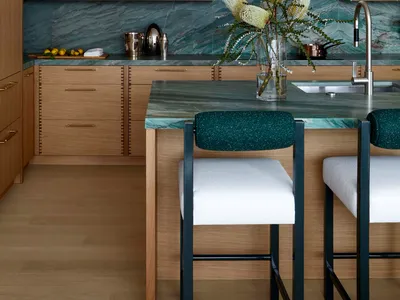 Modern kitchen featuring wooden cabinets with cane woven doors, green marble countertops and backsplash, and green upholstere