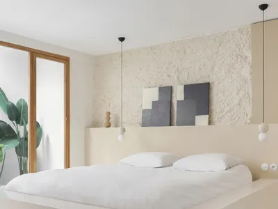 A minimalist bedroom with mixed materials, featuring a large bed with white bedding, a textured wall, and hanging light fixtu