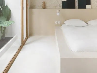 Minimalist bedroom with white walls, wooden flooring, and simple black and white artwork.
