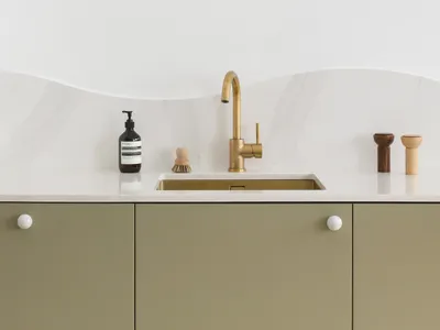 Modern minimalist kitchen featuring brass fixtures, green cabinetry, and white marble backsplash with three spherical wall sc