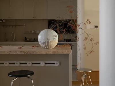 Minimalist kitchen with marble countertop and bar stools, featuring a large ceramic vase with intricate branch decorations.