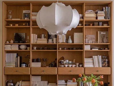 A modern home office featuring a wooden desk, chair, and bookshelves filled with books and decorative items.