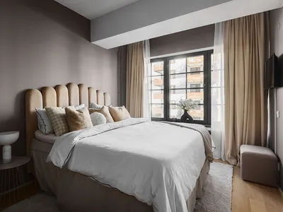 A minimalist bedroom with a white bed, beige headboard, and neutral-toned fabrics, featuring elegant decor and a view of a ci