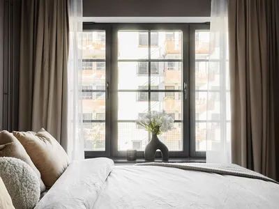 Modern bedroom with fabric bedding, white walls, and large window with curtains.