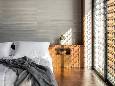 A minimalist bedroom with a wooden floor, white bedding, and a wooden nightstand with a small plant.