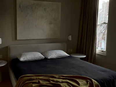 A neatly made bed with two white striped pillows and a dark blanket, featuring a large abstract artwork above it and a window