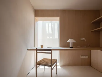 A minimalist home office with a wooden desk, chair, and bookshelf, featuring a clean and uncluttered design.