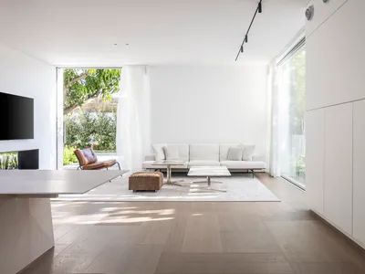 Modern minimalist living room featuring light wood flooring, marble coffee tables, and leather accent chair.