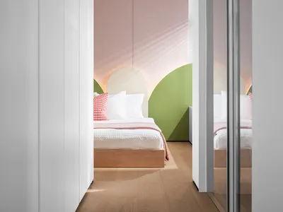 A minimalist bedroom with light-colored walls and white flooring, featuring a single twin bed with wood-textured headboard an