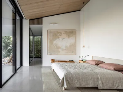 A minimalist bedroom featuring a modern wooden bed with pink pillows and a large abstract artwork on the wall.